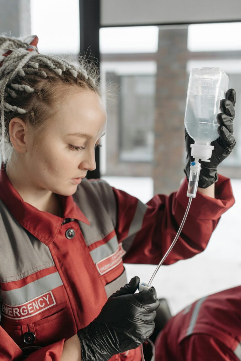 Female paramedic in red uniform preparing an IV drip for emergency medical care.
